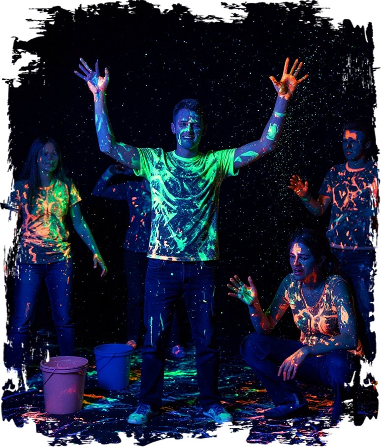 Four people covered head to toe in glowing neon paint under blacklight, arms raised mid-splatter